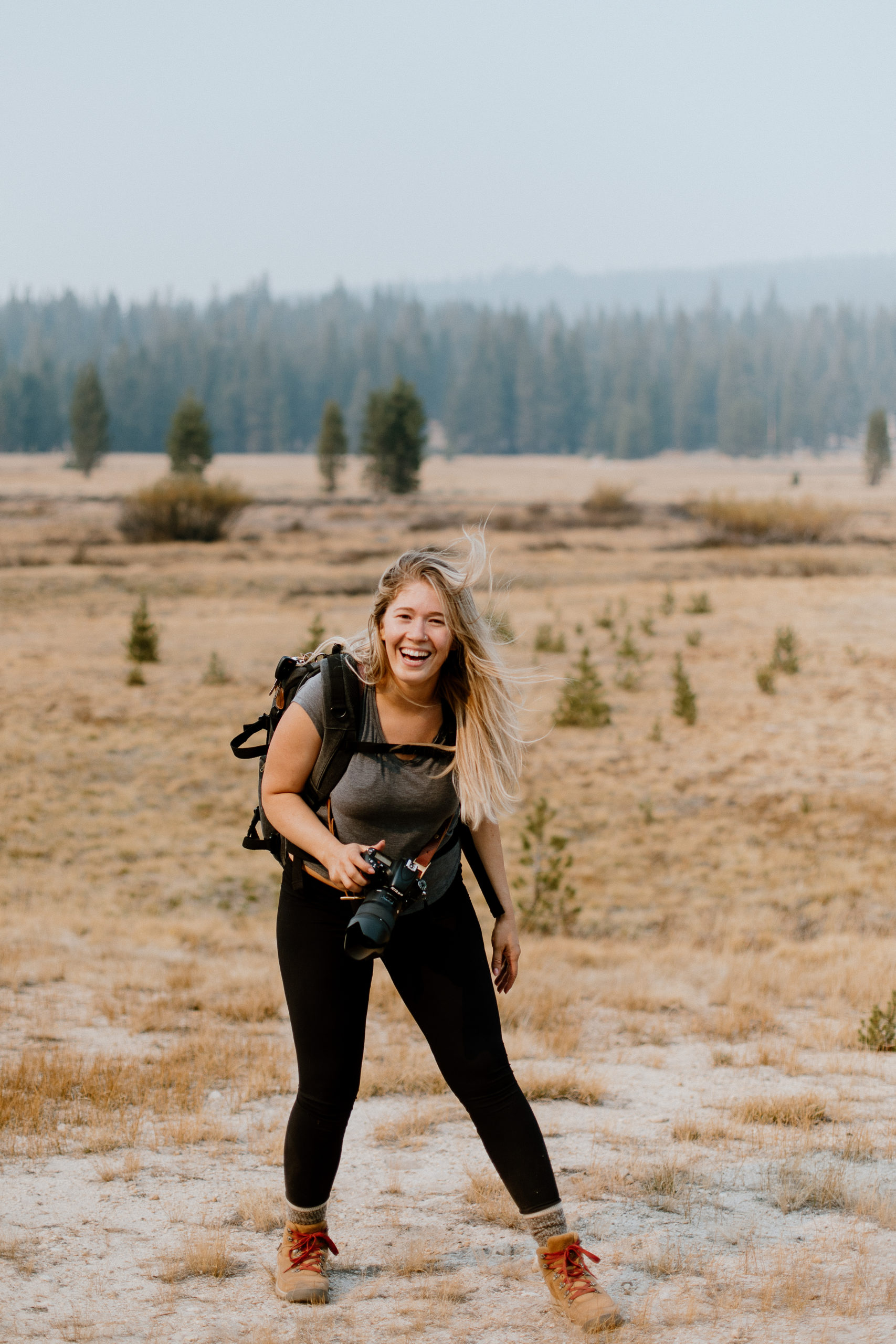 Girl holding camera while laughing with trees behind her