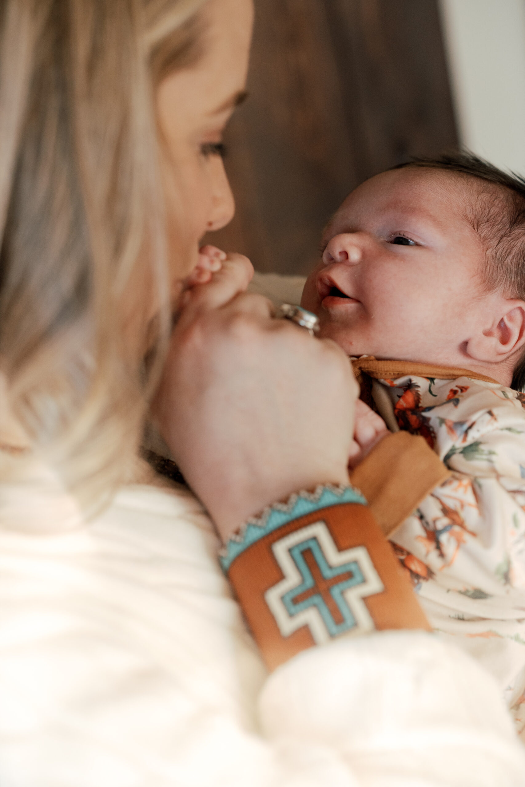 up close photo of mom holding baby and kissing his fingers, she is dressed in western fashion