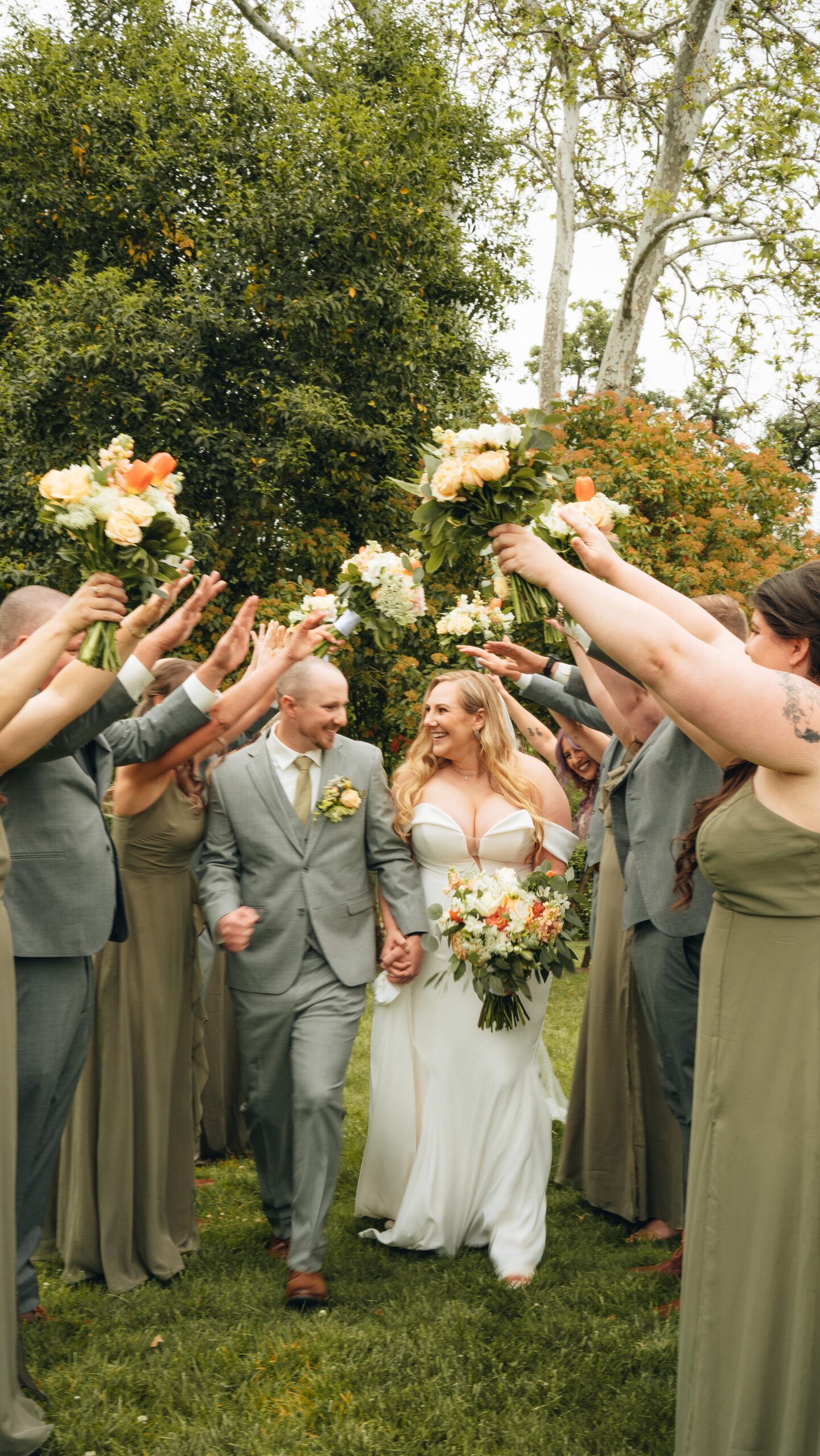bride and groom walking joyfully through a floral tunnel created by their wedding party, captured outdoors in natural light during an emotional wedding celebration
