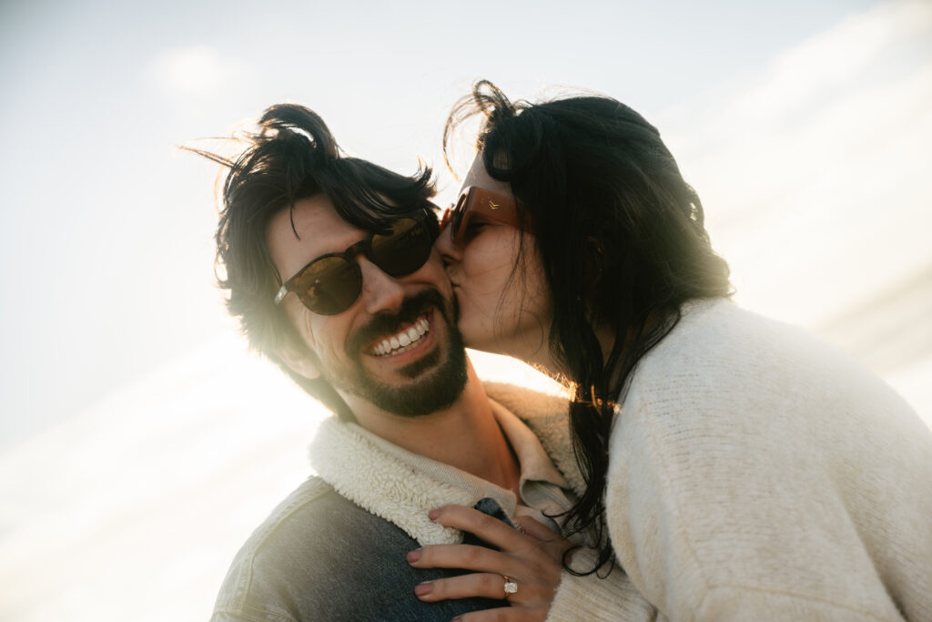 Man and woman kissing and smiling with wind in their hair on the beach