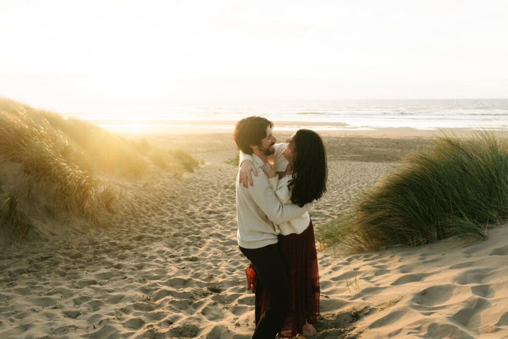 Couple hugging in sandy dunes with ocean behind them