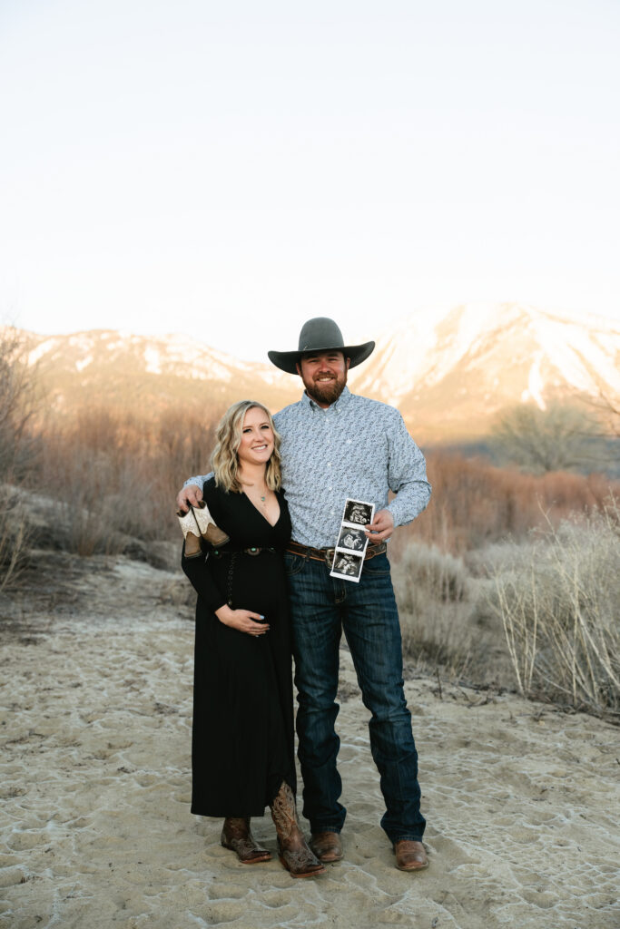 a man and woman standing next to each other holding a sonogram with a mountain view behind them
