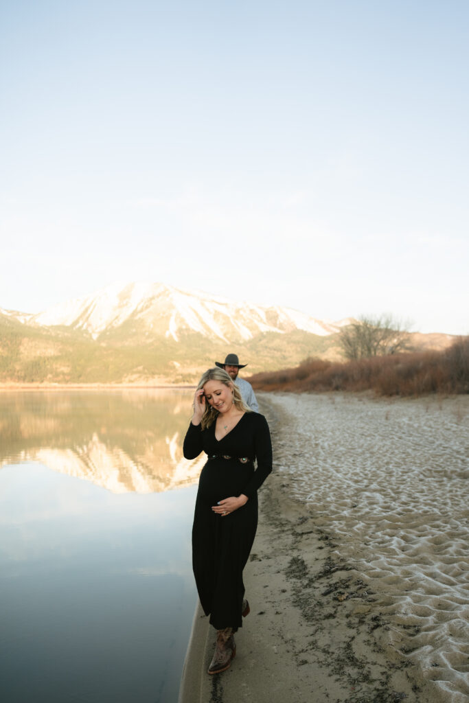 Photo of pregnant woman walking alongside lake with husband behind her