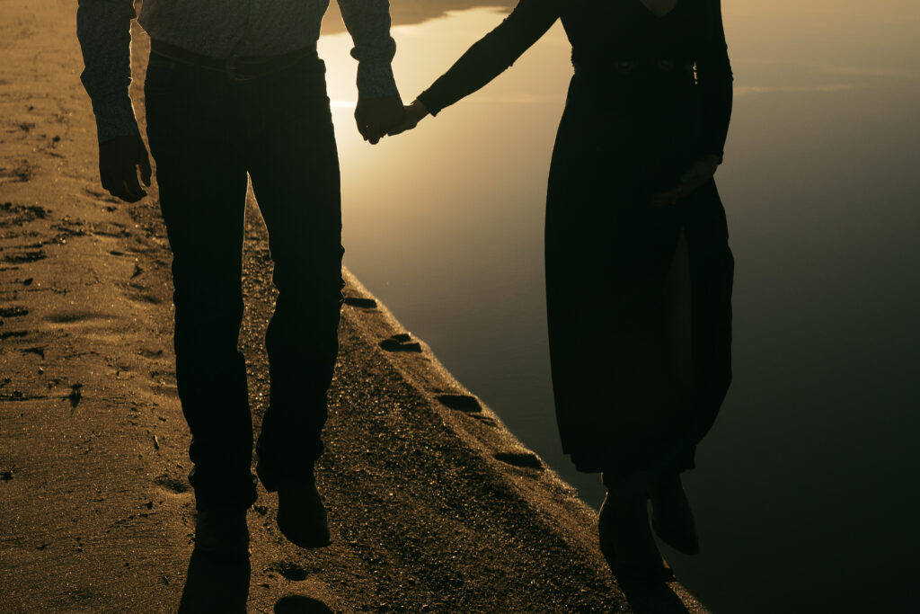 man and woman holding hands and walking next to a lake