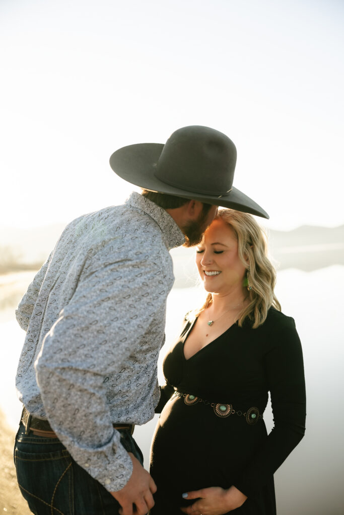 cowboy leaning in to kiss pregnant womans forehead